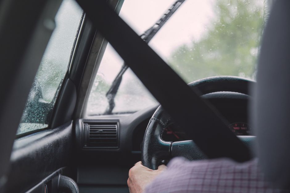 Pessoa dirigindo um veículo durante chuva, destacando o cuidado ao volante em condições adversas.