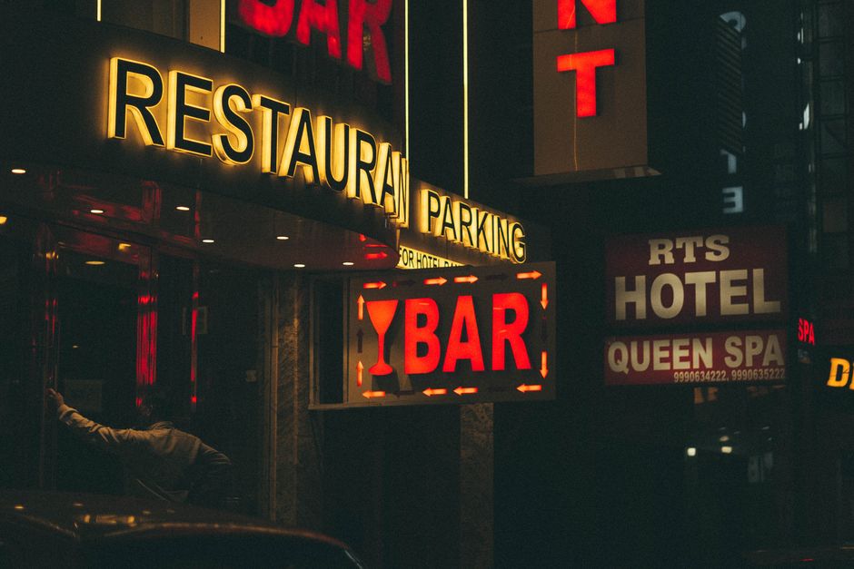 Sinalização nocturna de um bar e hotel em uma rua urbana, iluminada por luzes de néon vibrantes.