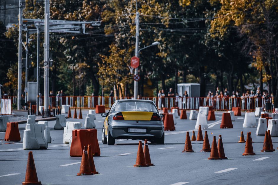 Imagem de uma rua fechada, com cones de trânsito e um carro trafegando, simular um circuito de testes ou treinamento veicular, ideal para artigos sobre trânsito, segurança veicular ou direção defensiva.