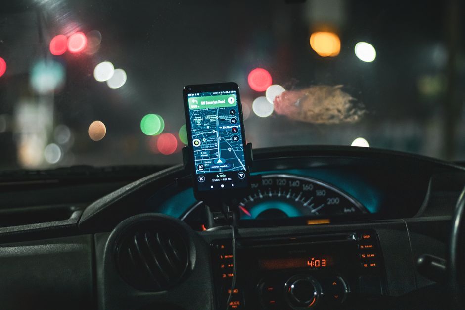 Imagem de um painel de carro com um telefone celular exibindo um aplicativo de navegação, capturada durante a noite na cidade.