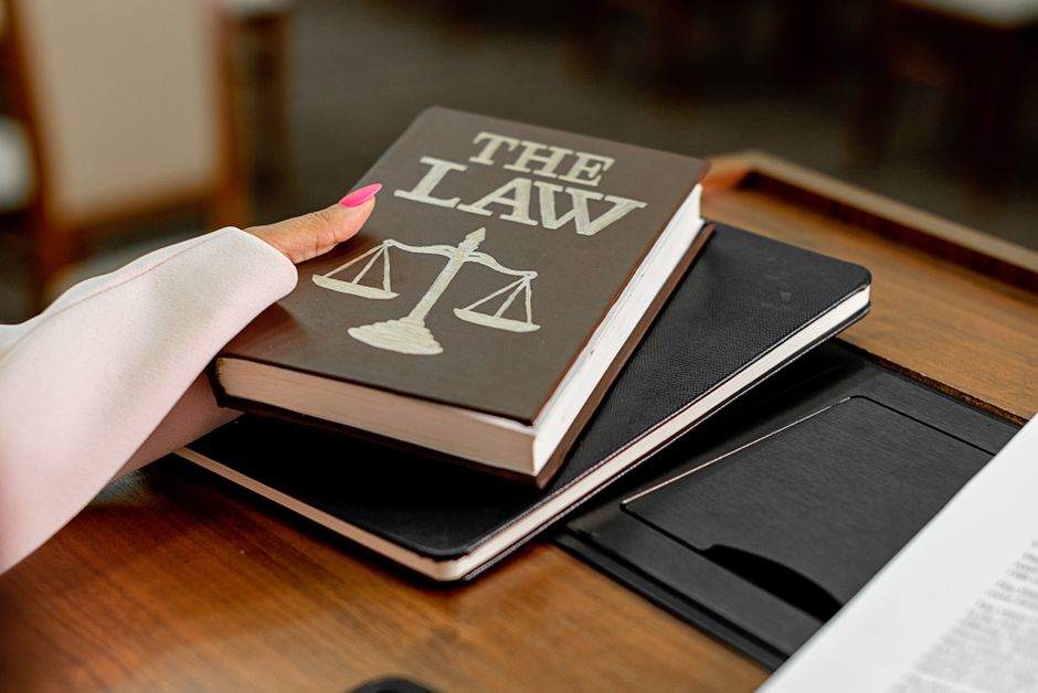 Imagem de um livro intitulado 'The Law' sobre assuntos jurídicos, com uma pessoa apontando, em um ambiente de estudo ou escritório.