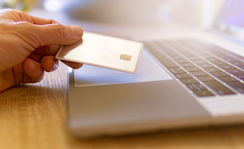 Pessoa realizando uma compra online usando cartão de crédito em um laptop, representando processos de pagamento digital.