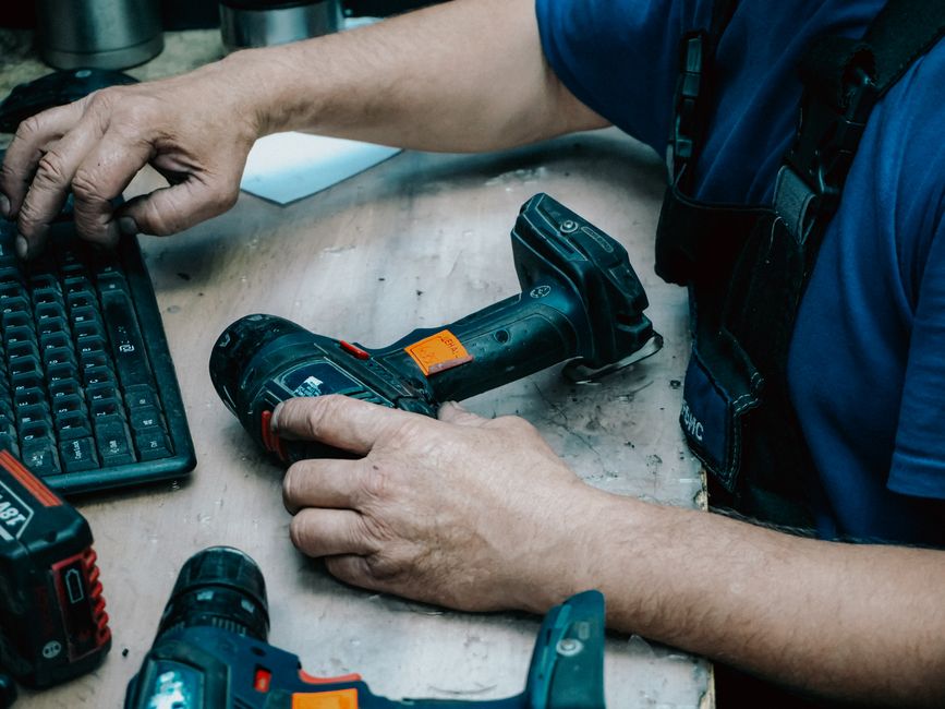 Homem ajustando uma ferramenta elétrica em um ambiente de trabalho técnico, demonstrando manutenção ou reparo de equipamentos.
