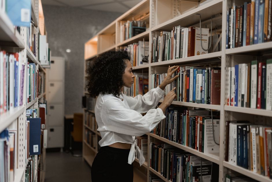 Mulher pesquisando livros em uma biblioteca, em um ambiente de estudos e pesquisa.