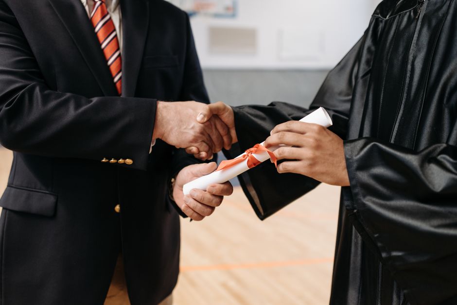 Jovem recebendo seu diploma de forma simbólica durante uma cerimônia de formatura, representando conquista acadêmica.