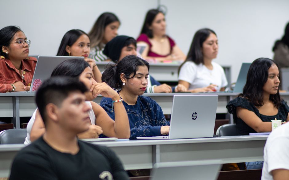 Mulheres estudantes participando de uma aula ou palestra em ambiente acadêmico ou de treinamento.