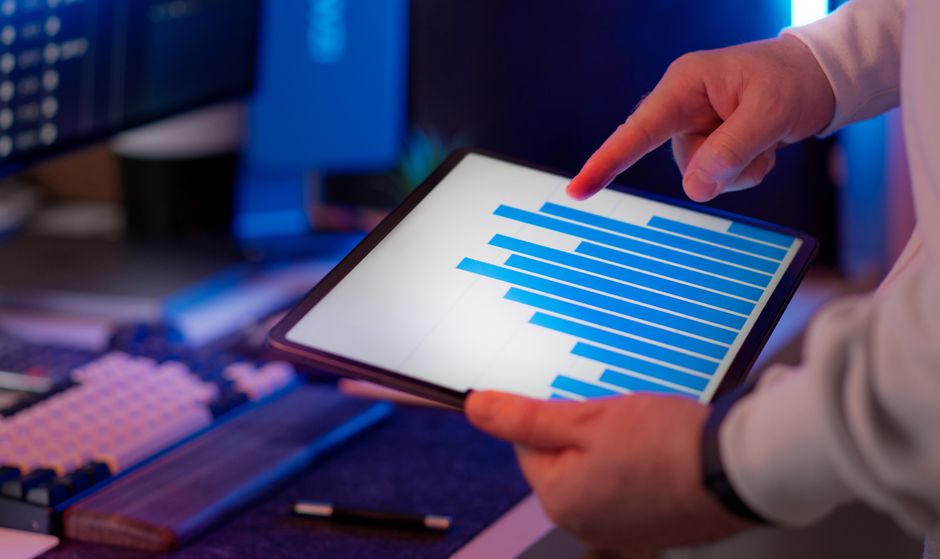 Pessoa analisando gráficos financeiros em um tablet, ilustrando estratégias de gestão e análise de dados empresariais.