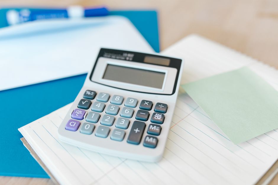 Imagem de uma calculadora sobre documentos e pastas, representando tarefas administrativas e financeiras em um ambiente de escritório.