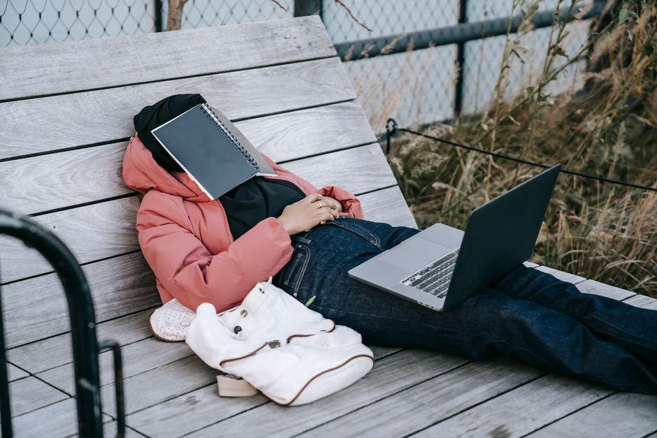 Pessoa descansando ao ar livre, usando um laptop para trabalho ou estudo, com materiais escolares ou profissionais ao seu alcance.