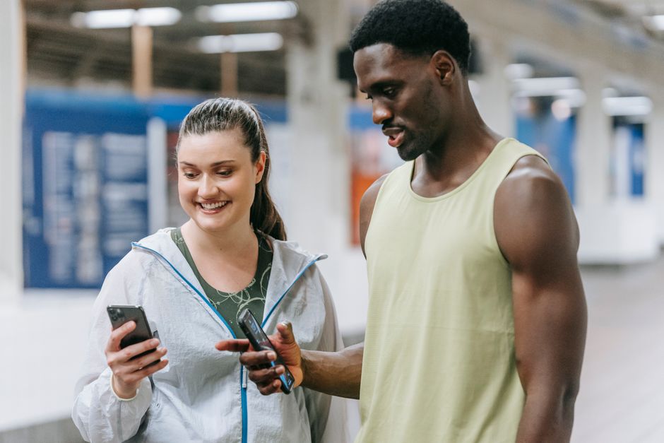 Homem e mulher compartilhando uma mensagem via celular em ambiente esportivo, indicando interação social ou motivação fitness.