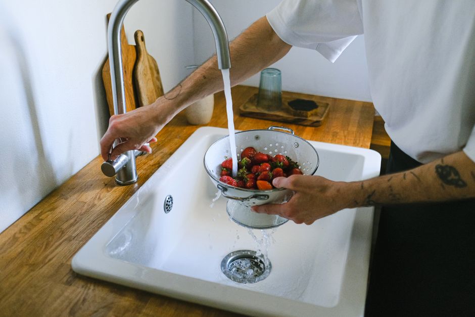 Pessoa lavando morangos em uma pia de cozinha, na preparação de alimentos frescos.