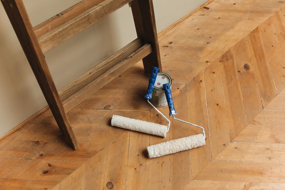 Imagem de um ambiente em reforma ou pintura, com um rolo de parede, uma lata de tinta e um escorador de madeira na sala, destacando a transformação do espaço.