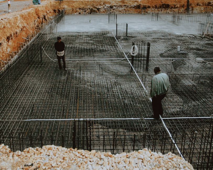 Sessão de inspeção na fase de fundação de uma construção civil, evidenciando a infraestrutura de concreto e armações de ferro.