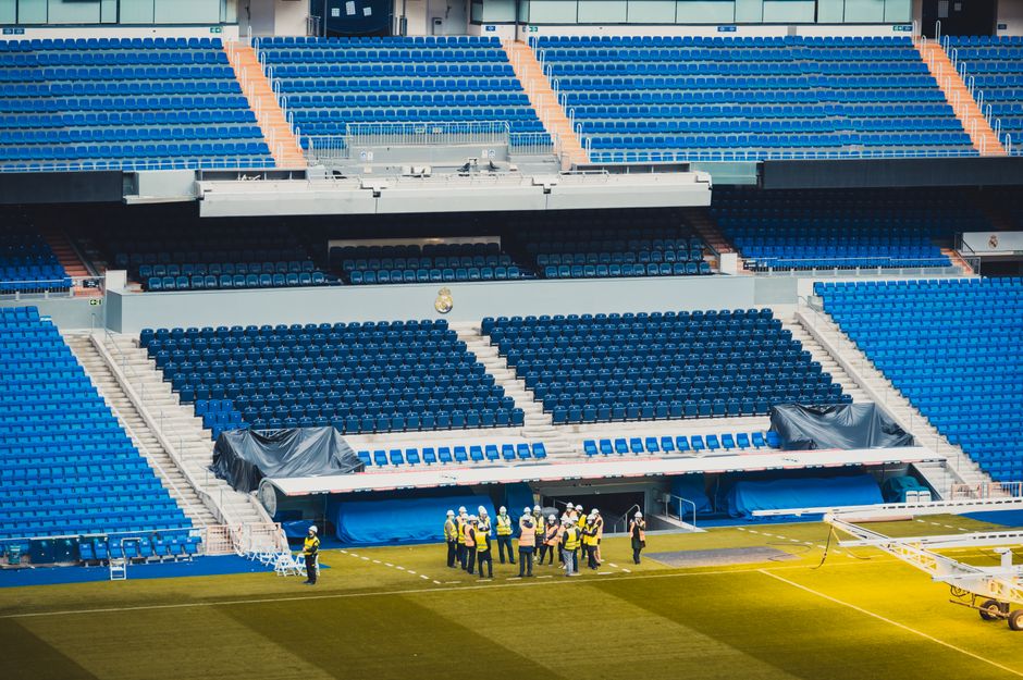 Grupo de trabalhadores realizando manutenção em estádio de futebol vazio, durante preparação para um evento esportivo.