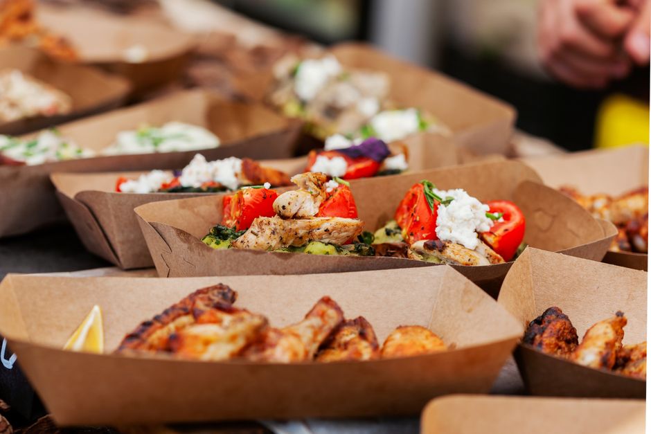 Imagem de pratos com comida, apresentando uma variedade de alimentos em embalagens sustentáveis, ideal para ilustrar uma refeição ao ar livre ou evento gastronômico.