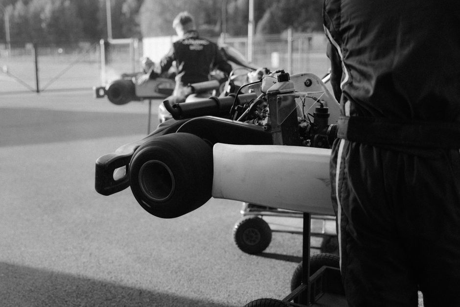 Imagem de duas pessoas preparando motos de fórmula 1 em uma pista ao ar livre, destacando o universo do automobilismo e preparação técnica.