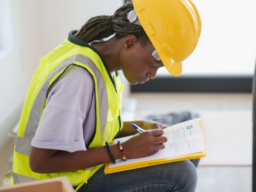 Mulher engenheira revisando documentos em ambiente de obra com foco em segurança e planejamento de construção.