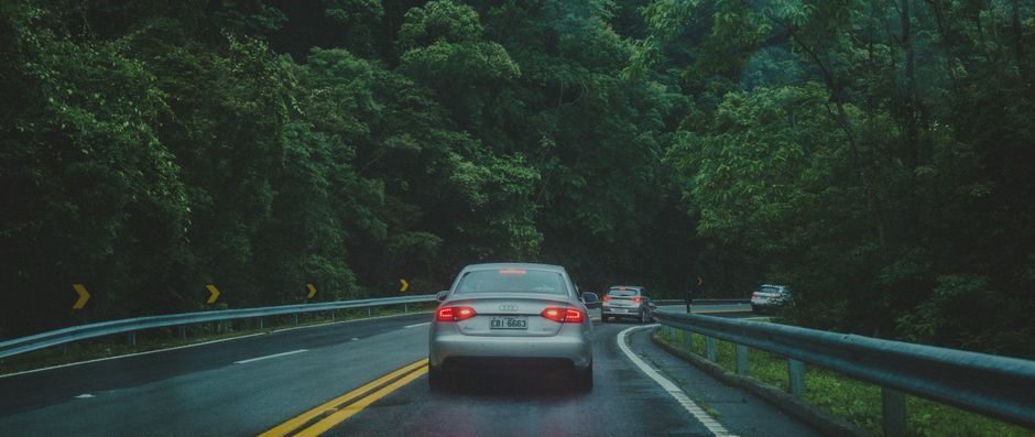 Imagem de uma rodovia sinuosa cercada por uma floresta densa, com veículos em movimento ao longo do caminho, sugerindo uma viagem ou percurso na natureza.