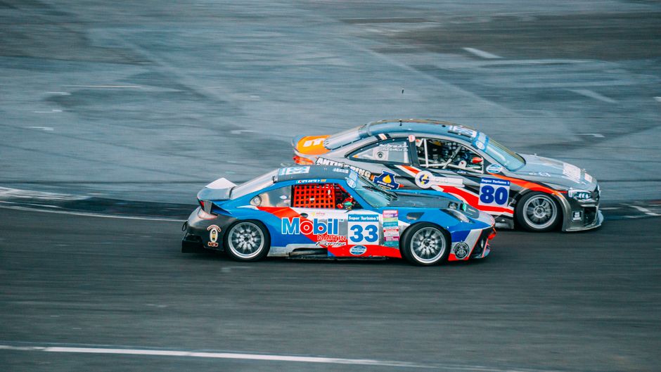 Carros de corrida em alta velocidade durante uma competição na pista, destacando o dinamismo e a emoção do esporte automotivo.