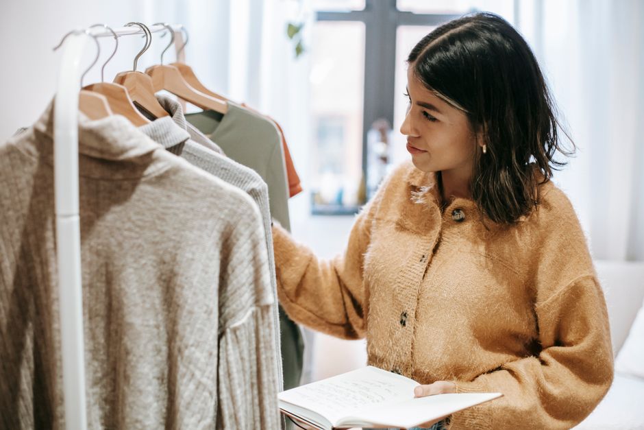 Mulher escolhendo roupas de inverno enquanto faz anotações, representando planejamento de compras ou seleção de wardrobe.