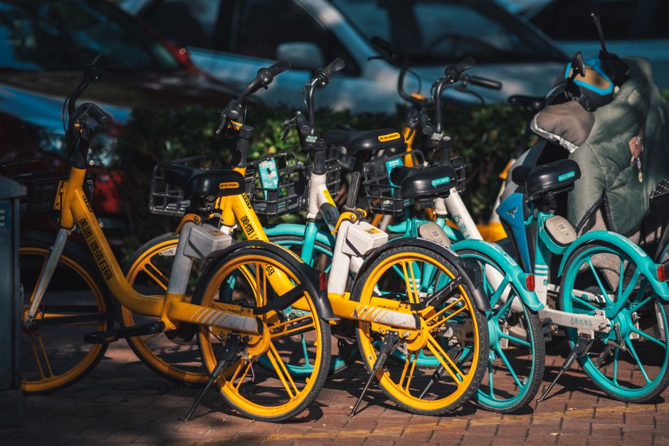 Foto de bicicletas de aluguel coloridas estacionadas em uma rua urbana, simbolizando mobilidade sustentável e transporte alternativo.