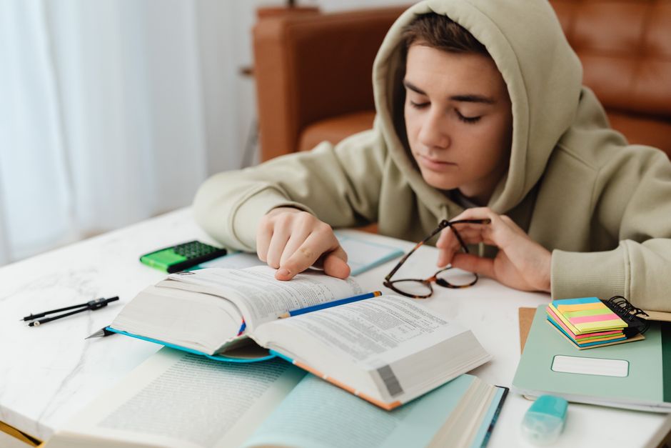 Jovem estudando com livros e materiais escolares sobre gestão de negócios e planejamento financeiro, em um ambiente de estudo.