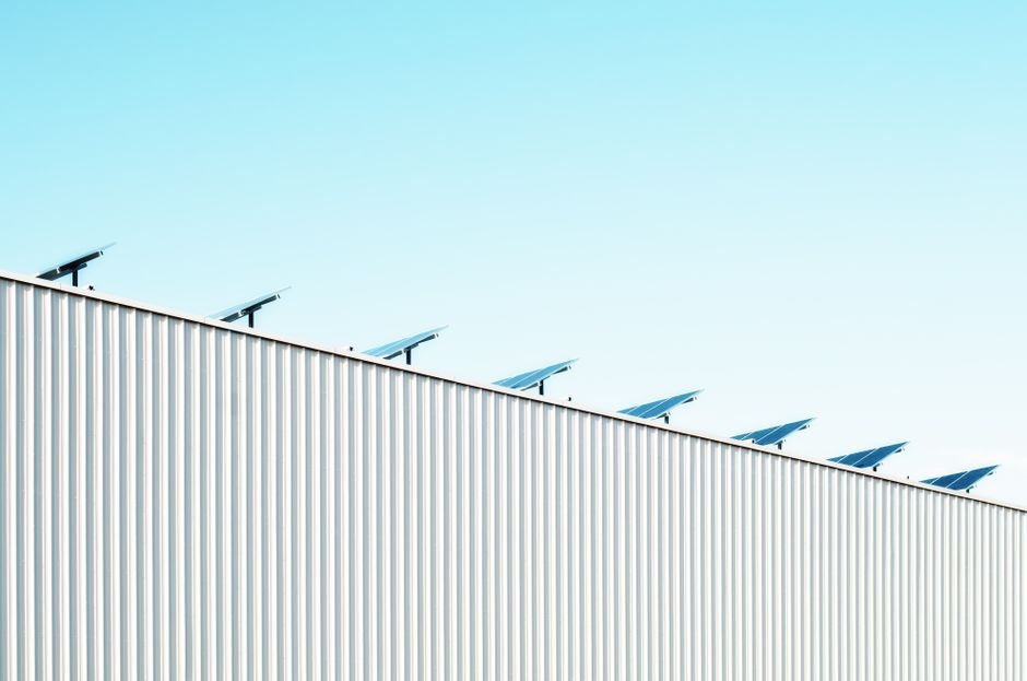 Imagem de painéis solares instalados no topo de uma estrutura industrial, refletindo tema de energia sustentável e inovação tecnológica.