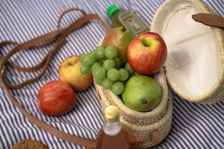 Imagem de uma cesta de picnic com frutas variadas sobre uma toalha listrada, transmitindo uma atmosfera de lazer ao ar livre.