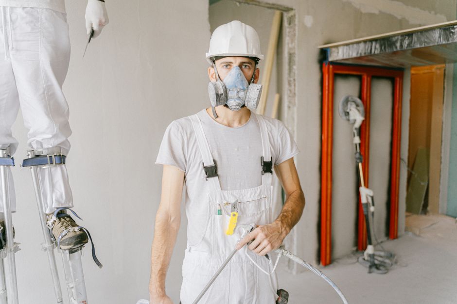 Imagem de um trabalhador da construção civil usando equipamento de proteção, em um ambiente de obra em reforma ou construção.