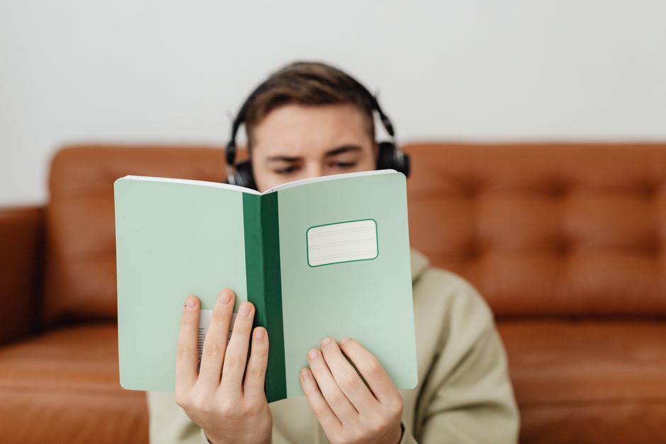 Jovem lendo um caderno enquanto usa fones de ouvido, em ambiente de estudo ou lazer.