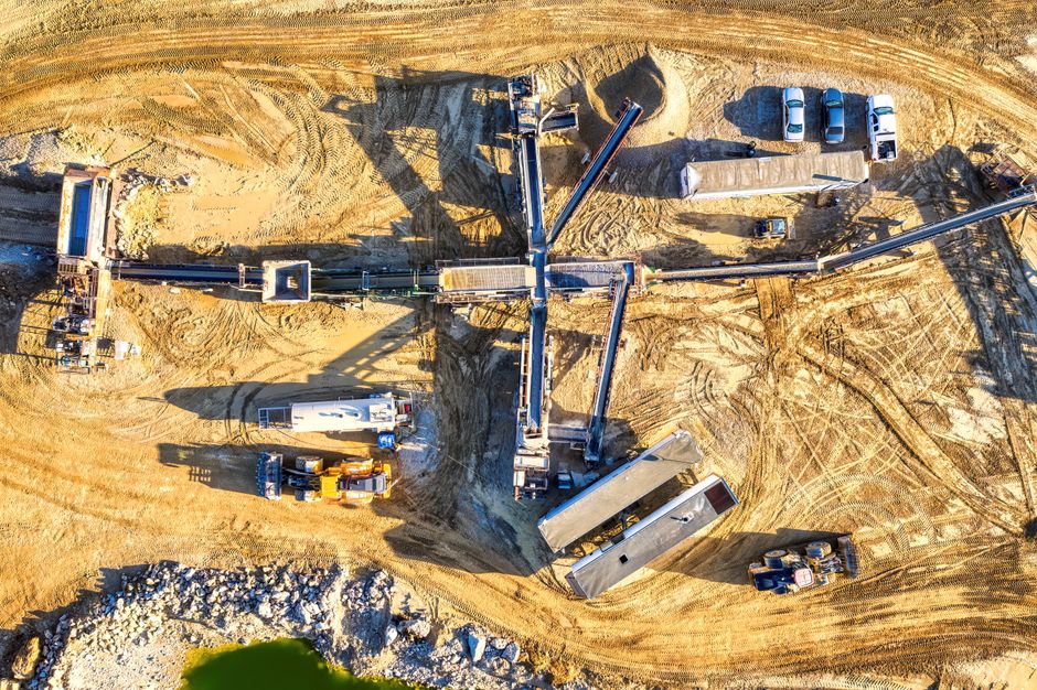 Imagem aérea de uma obra de mineração ou escavação, mostrando maquinário pesado em atividade na terra.
