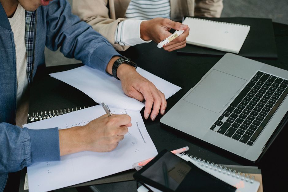 Pessoas discutindo planejamento financeiro em um ambiente de trabalho, com materiais de anotação, laptop e smartphone à mesa.