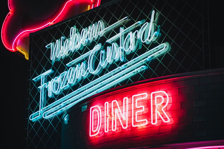 Letreiro neon com o nome de um restaurante ou lanchonete, iluminado à noite, transmitindo uma atmosfera urbana e moderna.