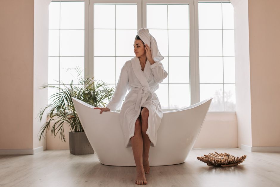 Mulher relaxando na banheira em um ambiente de spa ou banheiro com iluminação natural e decoração minimalista.