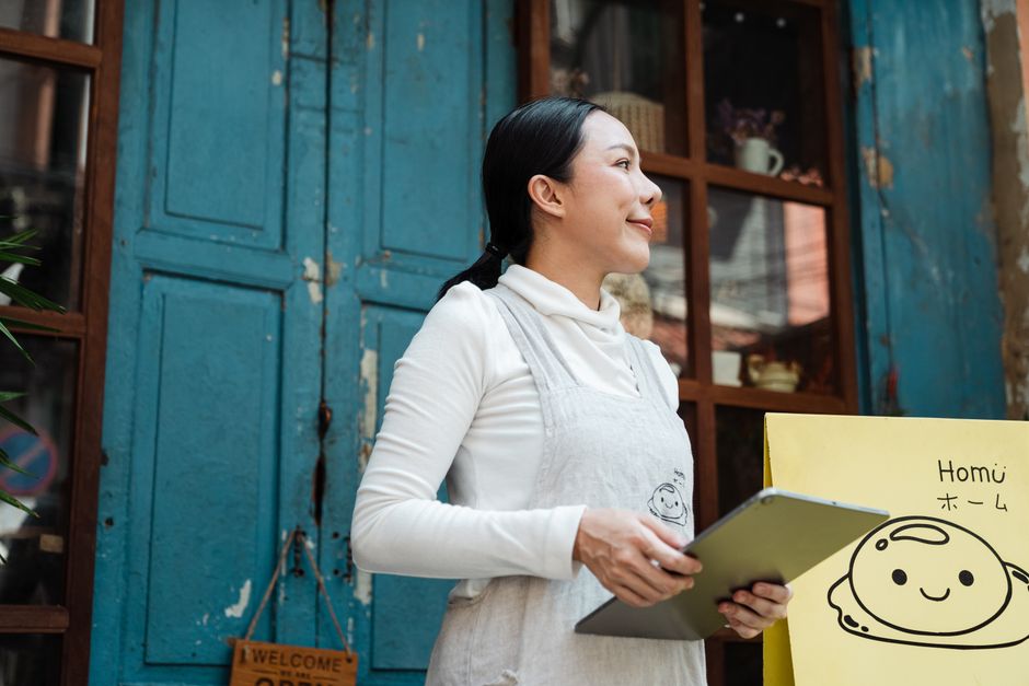 Mulher sorridente segurando um tablet, com uma parede azul de fundos e decoração rústica ao fundo, sugerindo um ambiente acolhedor e criativo.