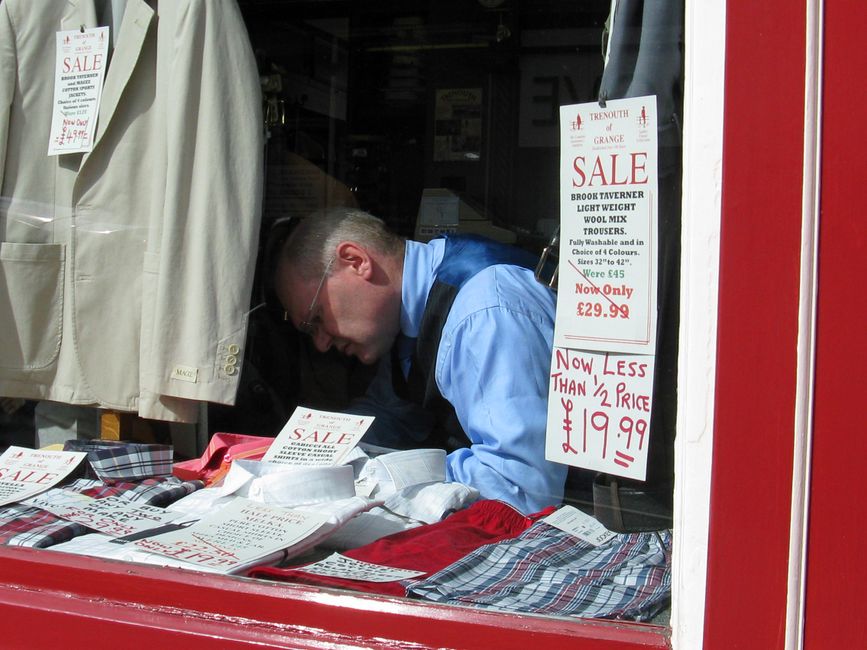 Vendedor organizando roupas em uma vitrine de loja durante uma liquidação.