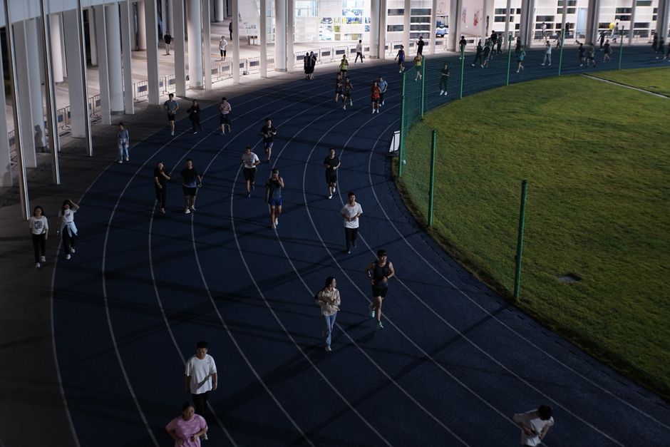 Grupo de pessoas correndo em uma pista de atletismo ao ar livre, promovendo saúde e atividade física em ambiente urbano.