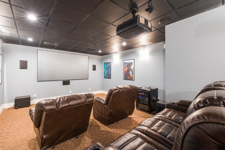 Sala de cinema em casa equipada com poltronas de couro, projetor e tela grande para entretenimento.
