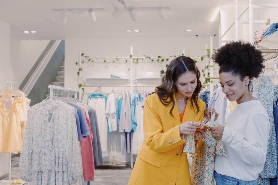 Duas mulheres analisando roupas em uma loja de moda feminina, evidenciando o tema de compras e moda casual.