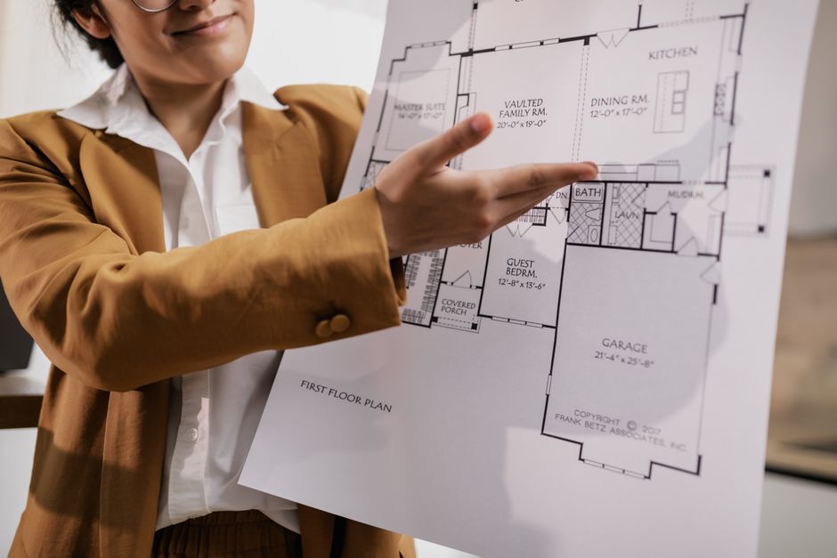 Pessoa analisando um projeto de planta de residência, refletindo sobre planejamento de construção ou design de interiores.