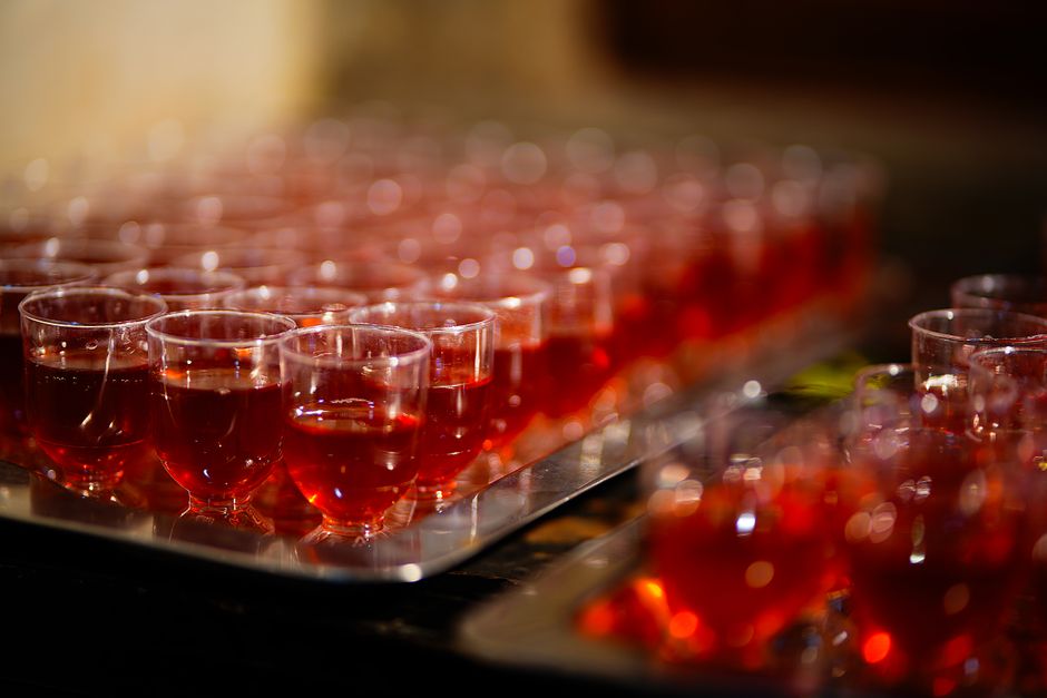 Grupo de pequenas taças de vinho tinto dispostas em uma bandeja, sugerindo um evento social ou degustação especializado.