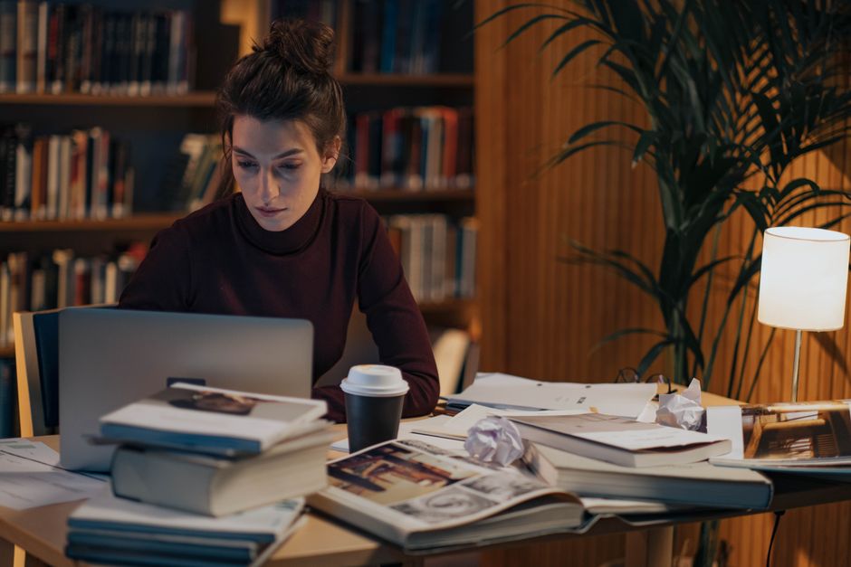 Mulher estudando ou trabalhando em um ambiente de leitura com várias anotações e livros, refletindo concentração e foco em estudos ou pesquisa.