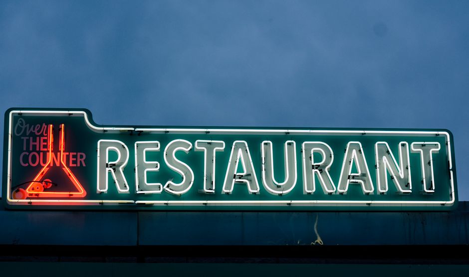 Placa de neon indicando um restaurante, com destaque para a iluminação e sinalização noturna.