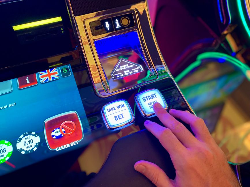 Jogador interagindo com uma máquina de caça-níquel em ambiente de cassino, destacando o tema de jogos de azar e entretenimento.