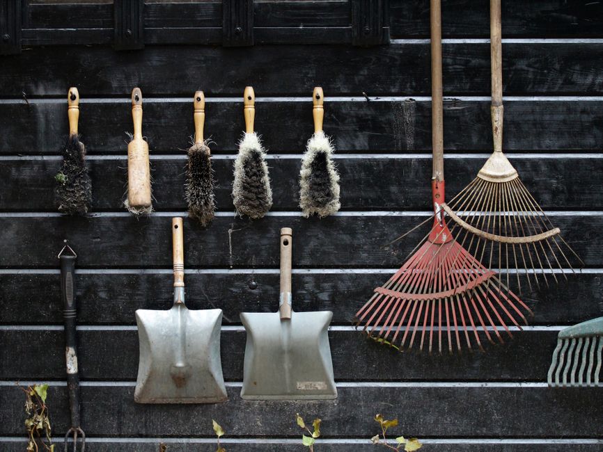 Ferramentas de jardinagem e limpeza penduradas em uma parede de madeira, prontas para uso no cuidado com o jardim ou tarefas domésticas.