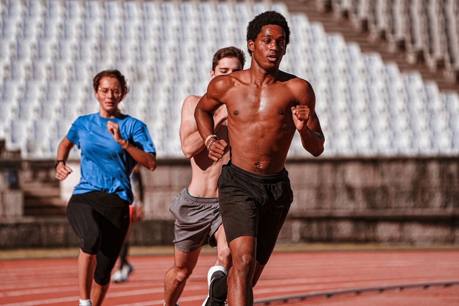 Grupo de jovens corredores treinando em uma pista de atletismo ao ar livre, direcionados e focados no esforço físico.