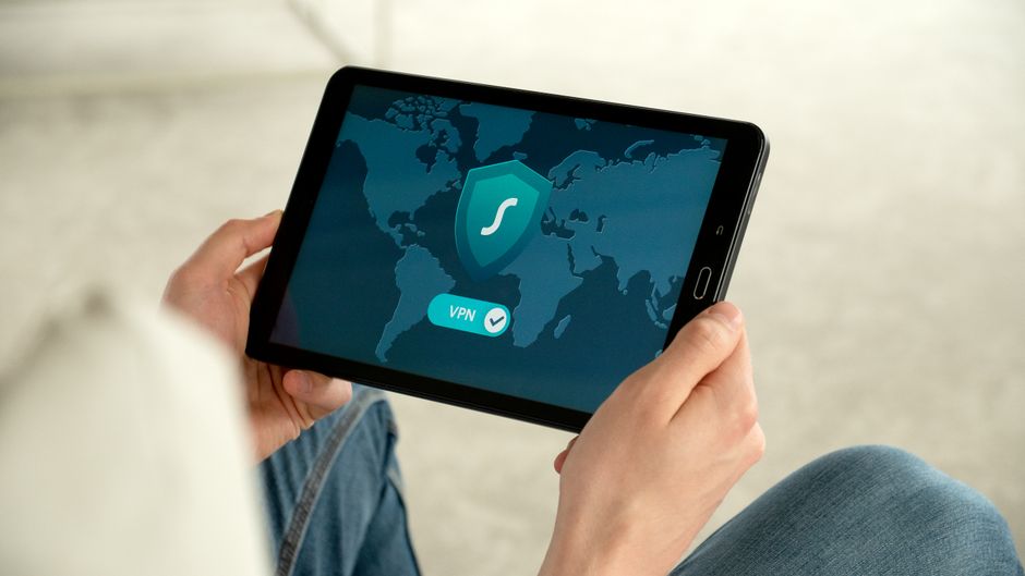 Pessoa segurando um tablet com um símbolo de VPN e um escudo, representando segurança digital e privacidade online.