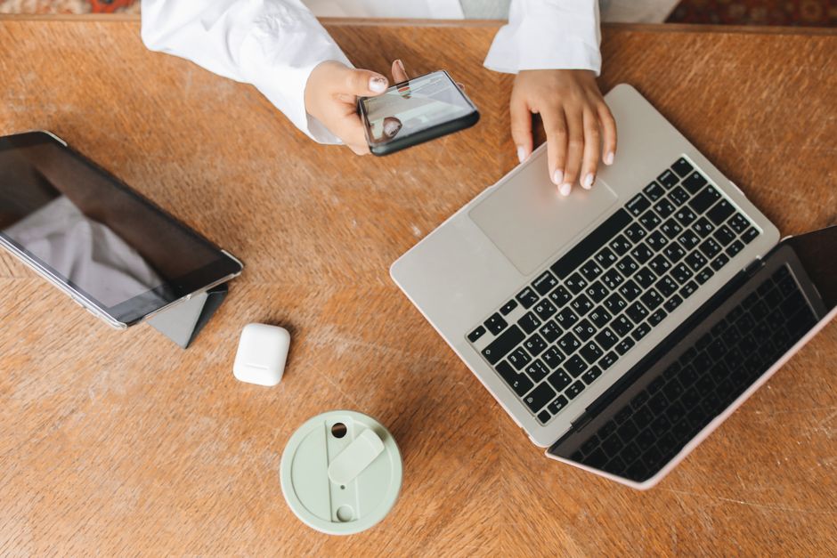 Imagem de uma pessoa utilizando um celular e um laptop em uma mesa de trabalho, simbolizando produtividade e tecnologia no ambiente de escritório.