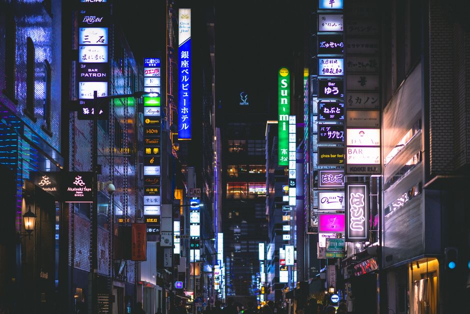 Cena noturna de uma rua urbana iluminada por letreiros de neon, refletindo a vibrante vida noturna de uma cidade movimentada.