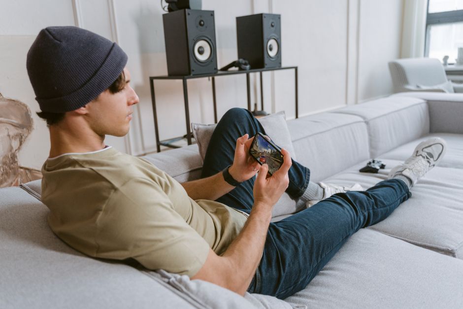 Homem relaxando em um sofá de casa, jogando videogame em um ambiente de entretenimento doméstico.